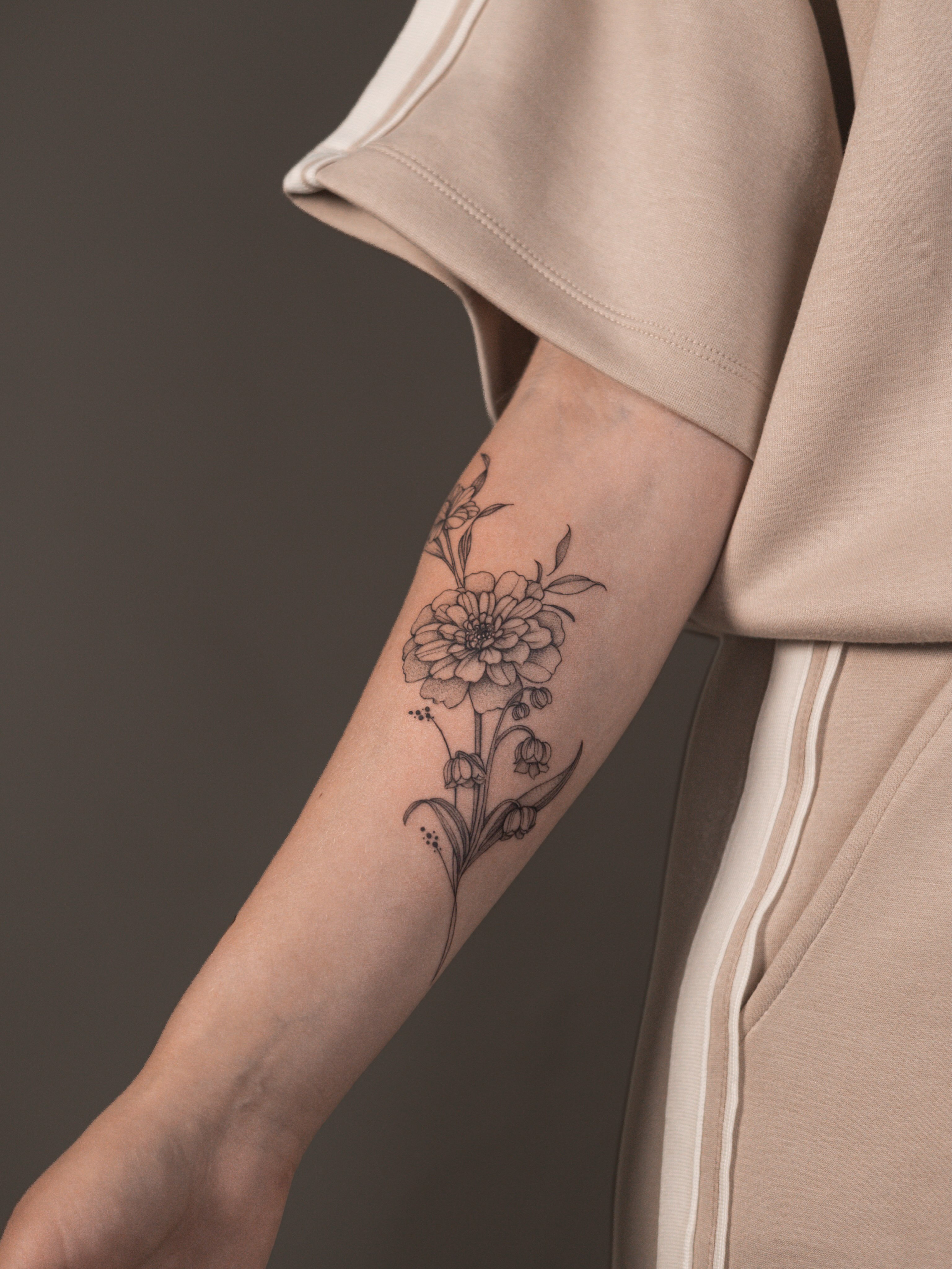 Fine-line geboortebloem tattoo met verschillende bloemen op de onderarm