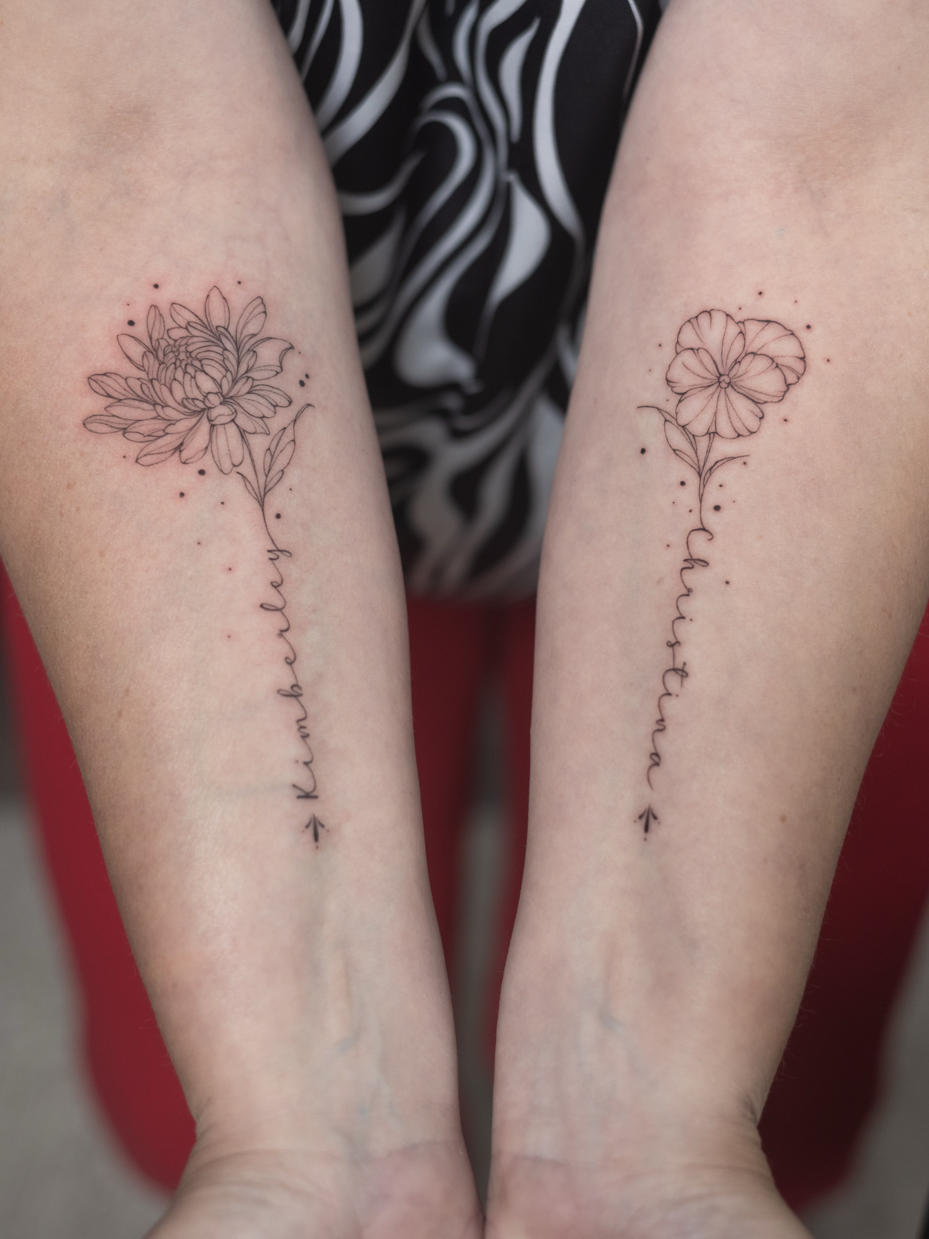 Twee matching fine-line tattoos met de geboortebloemen van dochters